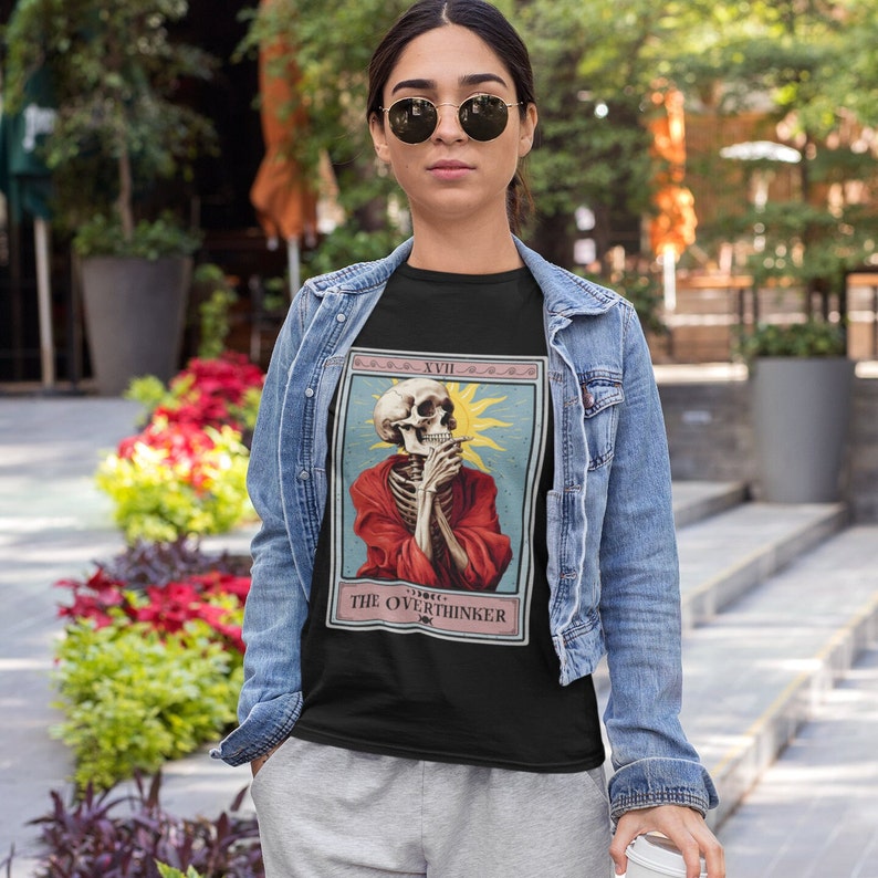 May include: Black t-shirt with a vintage tarot card design featuring a skeleton in a red robe with the text "XVIII THE OVERTHINKER".