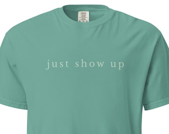 以下が含まれることがあります： 「just show up」の文字が薄いグレーでプリントされた、半袖のシーフォームグリーンのTシャツ。クルーネックでリラックスしたフィット感があり、カジュアルウェアに適しています。