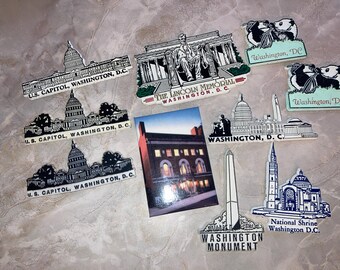 Pode incluir: Uma coleção de lembranças com o tema Washington, D.C., incluindo ímãs e um cartão-postal. Os itens apresentam ilustrações do Capitólio dos EUA, Lincoln Memorial, Washington Monument, National Shrine e pandas, com legendas para cada marco.