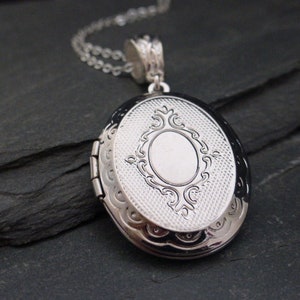 Può includere: Collana con ciondolo ovale in argento con un design floreale dettagliato. Il ciondolo ha un'apertura a cerniera e una finitura liscia e lucida.