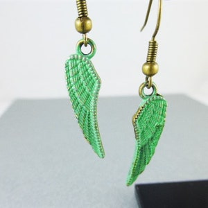 May include: A pair of green angel wing earrings with a bronze finish. The wings are detailed with a textured pattern.