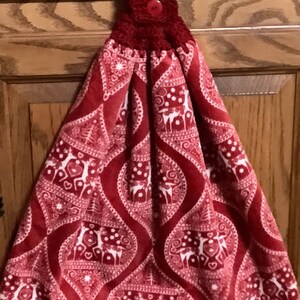 May include: Red kitchen towel with a white snowflake and reindeer pattern. The towel has a crocheted red loop with a red button.