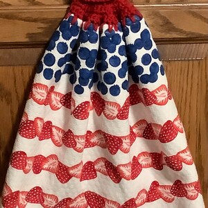 May include: Red, white, and blue kitchen towel with a crocheted hanging loop and a white button. The towel features a pattern of strawberries and blueberries.