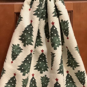 May include: A hanging kitchen towel with a green crocheted top and a red button. The towel features a white background with a repeating pattern of green Christmas trees with red star toppers. A festive holiday kitchen accessory.