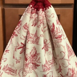 May include: A red crocheted dish towel with a button and a white fabric with a red floral pattern.