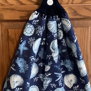 May include: A blue kitchen towel with a seashell pattern and a navy blue crocheted loop with a white button.