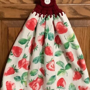May include: A white kitchen towel with a red button and a burgundy crocheted loop. The towel has a watercolor pattern of strawberries and leaves.