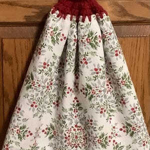 May include: A white kitchen towel with a red berry and green leaf pattern. The towel has a red crocheted loop with a white button.