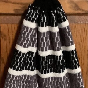 May include: A black and white striped kitchen towel with a gray pattern. The towel has a loop at the top and a white button.