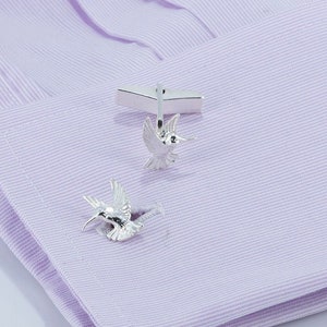 May include: A pair of silver hummingbird cufflinks on a light purple shirt.