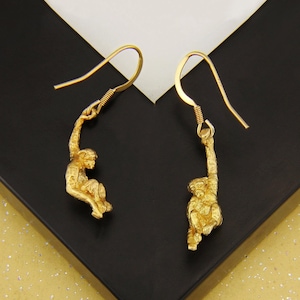 May include: A pair of gold earrings featuring a monkey design. The monkeys are hanging from the earrings and have a detailed, realistic look.
