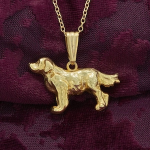 May include: A gold-colored pendant necklace featuring a detailed, three-dimensional dog charm. The dog is standing with its head turned to the side, and its tail is curled up.