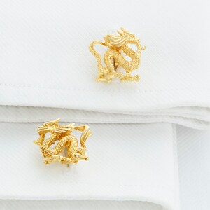 May include: A pair of gold cufflinks featuring a detailed dragon design.