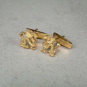 May include: A pair of gold-tone cufflinks featuring a detailed dragon design. The cufflinks are connected by a simple bar.