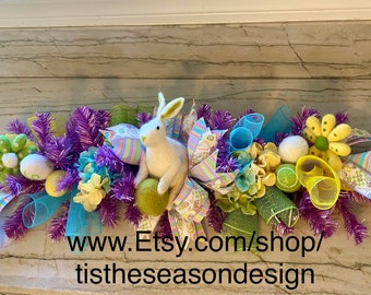 May include: A colorful Easter garland with a white bunny, yellow flowers, green and blue ribbons, and purple tinsel. The garland is on a marble countertop. www.Etsy.com/shop/tistheseasondesign