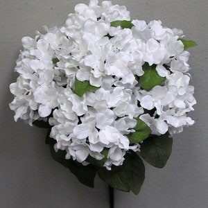 Puede incluir: Un ramo de hortensias artificiales blancas con hojas verdes. Las flores están dispuestas en un racimo y tienen un aspecto realista.