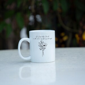 May include: White ceramic mug with a curved handle. The mug features a black floral design and the text "So Casually Chic in the Name of Being Honest". The mug is sitting on a white surface.