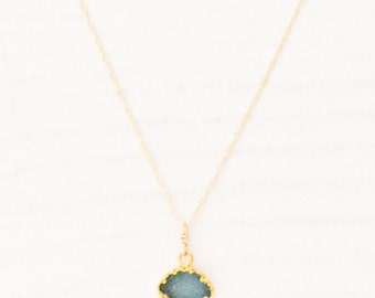 May include: A delicate gold chain necklace with a small, blue gemstone pendant. The pendant has a gold-toned, scalloped edge.