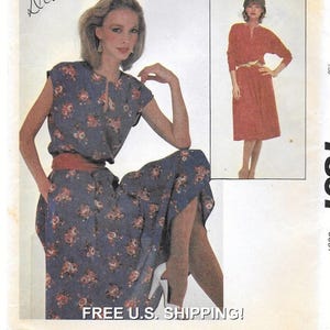 Puede incluir: Un patrón de costura vintage que presenta a una mujer con un vestido floral azul con un cinturón a juego. El vestido tiene un escote de ojo de cerradura y mangas cortas. También se muestra un segundo vestido de color óxido.