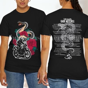 May include: Black t-shirt with a snake, motorcycle, and rose graphic on the front. The back of the shirt displays the text "To Be Loved By Kade Mitchell" with a snake and rose design and additional text.