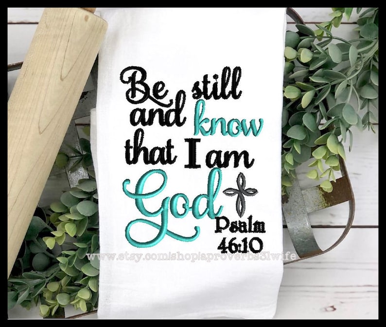 May include: White kitchen towel with teal blue embroidery that reads "Be still and know that I am God" with a small cross and the text "Psalm 46:10" below.