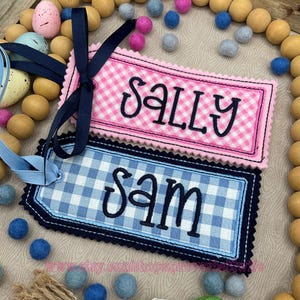 May include: Two personalized fabric gift tags with blue and white gingham and pink and white gingham patterns. The tags are embroidered with the names "Sam" and "Sally".