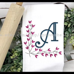 Puede incluir: Toalla de cocina bordada con una letra A azul marino y un dise&ntilde;o floral rosa. La toalla es blanca y tiene un dise&ntilde;o simple y elegante.
