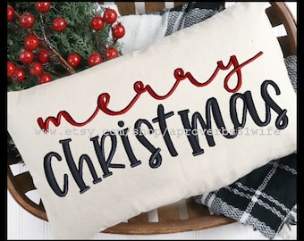 Puede incluir: Una almohada blanca con las palabras "merry christmas" bordadas en negro y rojo. La palabra "merry" está en cursiva roja y la palabra "christmas" está en letras mayúsculas negras.