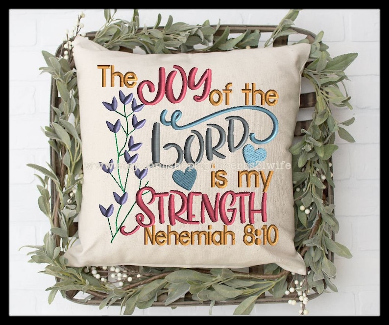 May include: A white pillow with the text "The Joy of the Lord is my Strength Nehemiah 8:10" embroidered in colorful thread. The pillow is decorated with purple flowers and blue hearts.