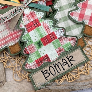 May include: Christmas tree-shaped felt ornaments with red and green plaid patterns. Each tree has a green border and a brown base. One ornament has a rectangular tag that says "BOMAR" in black letters.