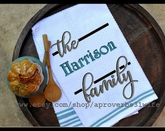 May include: White kitchen towel with blue and gray embroidery that reads "The Harrison Family".