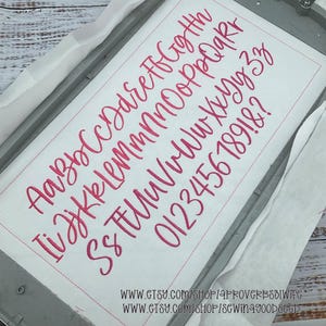 May include: A white fabric with a pink embroidered cursive alphabet, numbers, and symbols. The letters are in uppercase and lowercase. The fabric is held in a metal embroidery hoop. The image includes the text: WWW.ETSY.COM/SHOP/APROVERBS31WIFE and WWW.ETSY.COM/SHOP/SEWINGGOODSEED.