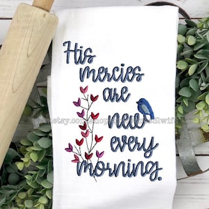 May include: White kitchen towel with blue embroidery that reads "His mercies are new every morning". A small blue bird is embroidered on the right side of the towel. Pink and red hearts are embroidered on a stem to the left of the text.
