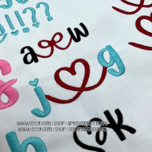 May include: Close-up of embroidered letters and symbols in various colors on a white fabric. The letters include black, pink, and teal, with a red heart-shaped design. The image also includes the text: www.etsy.com/shop/aproverbs31wire and www.etsy.com/shop/sewingoodseco.