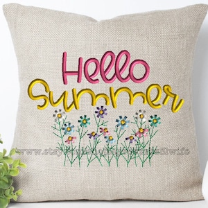 Puede incluir: Una almohada beige con el texto "Hello Summer" bordado en rosa y amarillo. El texto está rodeado por una fila de flores bordadas en varios colores.