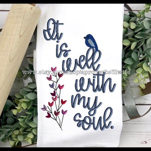 Könnte beinhalten: Weißes Küchentuch mit blauer Stickerei, auf der "It is well with my soul" steht. Ein kleiner blauer Vogel befindet sich über dem Text und ein Zweig mit rosa und violetten Blüten befindet sich links vom Text.