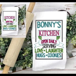 Könnte beinhalten: Weißes Küchentuch mit gesticktem Text, der "Bonny's Kitchen Open Daily Serving Love Laughter Hugs Cookies" lautet.