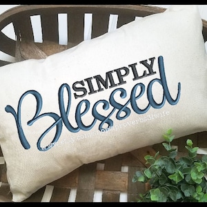 May include: A white pillow with the text "SIMPLY BLESSED" embroidered in blue and black lettering.