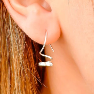 May include: Silver spiral earrings with a hammered texture. The earrings are shown on a person's ear.