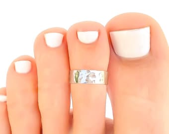 May include: A silver toe ring with a hammered texture. The ring is worn on the second toe of a foot.