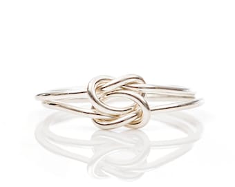 May include: A silver-colored ring featuring a knot design. The ring has a double band and a polished finish, reflecting light. The knot is the focal point, creating a unique and elegant piece of jewelry.