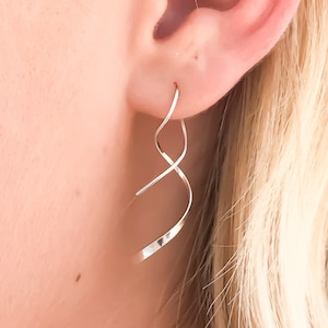 May include: Silver-toned spiral drop earrings. The earrings feature a continuous, flowing shape made from thin, curved metal. The design is minimalist and modern, with a hammered texture on the lower section. A stylish accessory.