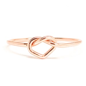 May include: A rose gold ring with a heart-shaped knot design.