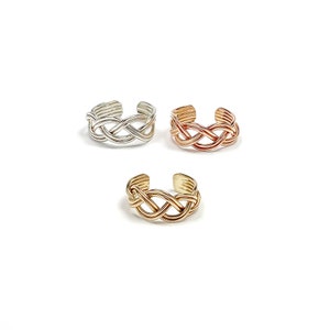May include: Three adjustable toe rings in silver, rose gold, and gold. Each ring features a woven, braided design. The rings are displayed on a white background, showcasing their intricate details and metallic finishes.