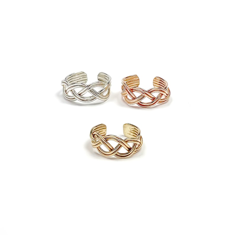May include: Three adjustable toe rings in silver, rose gold, and gold. Each ring features a woven, braided design. The rings are displayed on a white background, showcasing their intricate details and metallic finishes.
