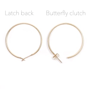 May include: A pair of gold hoop earrings with a latch back closure on the left and a butterfly clutch closure on the right.