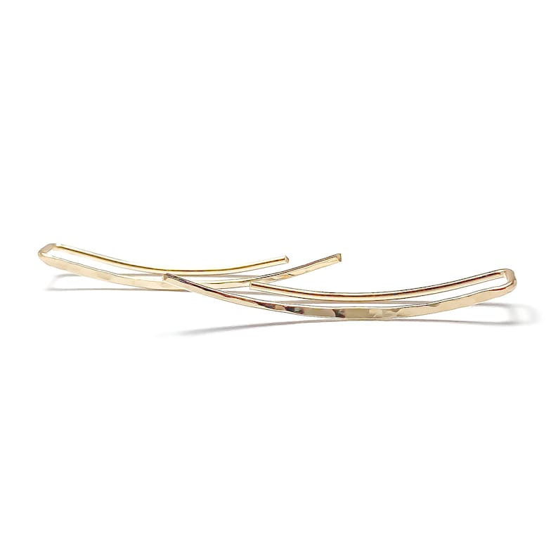 May include: A pair of gold-toned, hammered, curved earrings. The earrings are simple and minimalist in design.