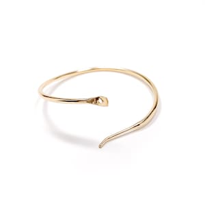 May include: A gold-toned, open circle bangle bracelet with a single, thin, pointed end.