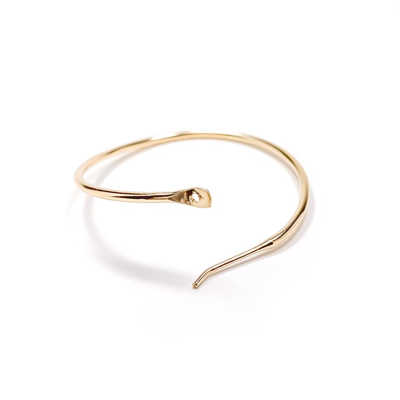 May include: A gold-toned, open circle bangle bracelet with a single, thin, pointed end.