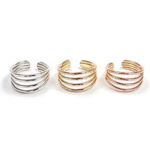 May include: Three open-style rings arranged in a row, each featuring four stacked bands with a hammered texture. The rings are finished in silver, gold, and rose gold tones, showcasing a multi-layered design with a gap at the back.